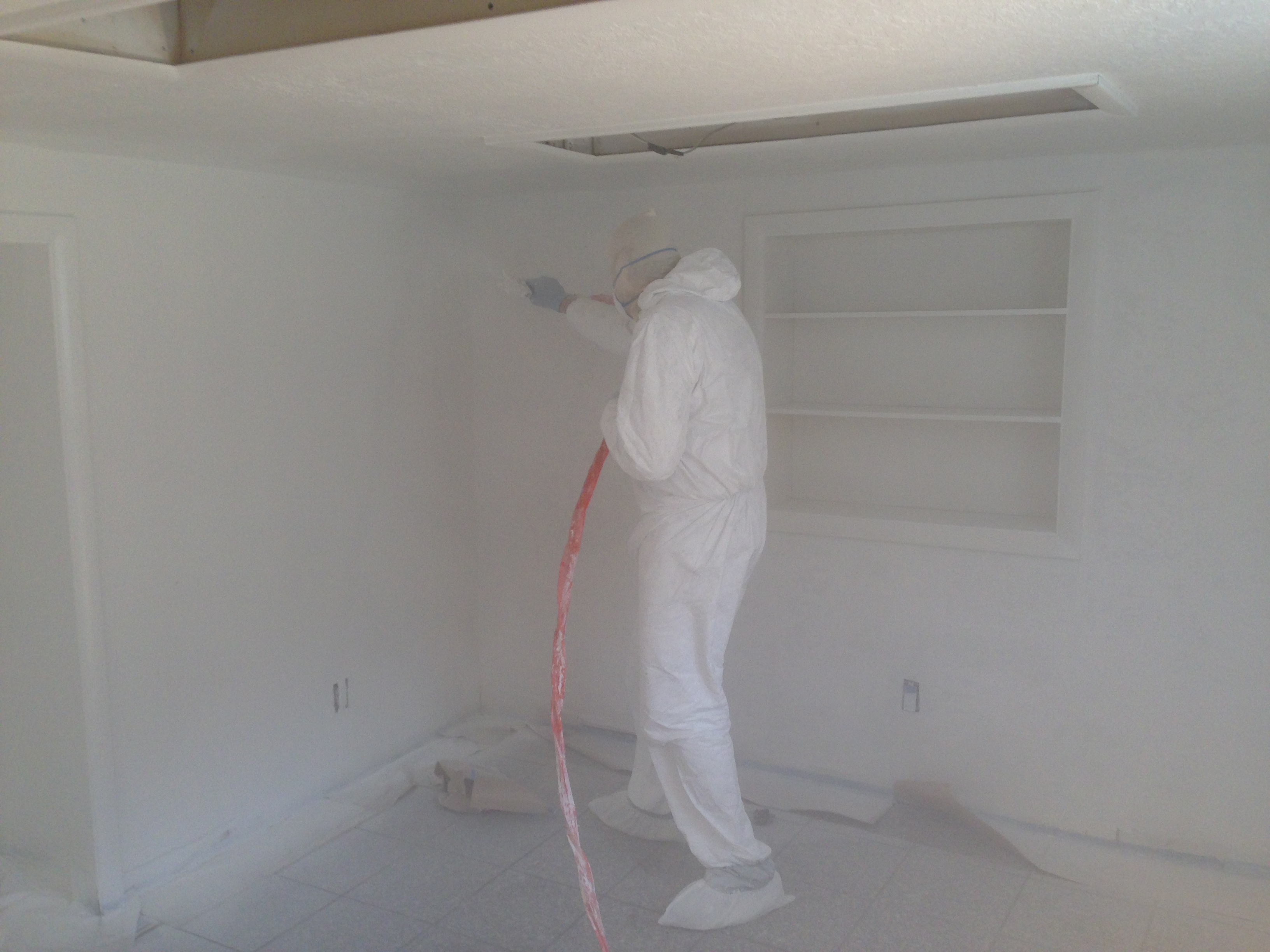 Painter in protective suit spray-painting interior walls